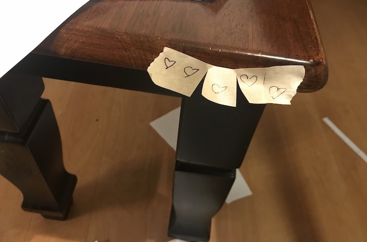 Image shows a closeup of the other end of the bench with five small pieces of masking tape still attached at the top. On them are one or two outlined hearts. 