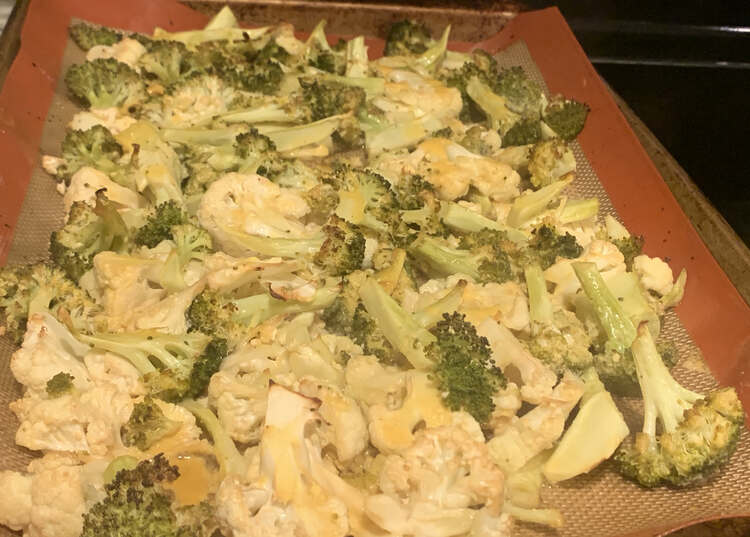 Image shows an orange silpat sheet covered in yellow tinged cauliflower and broccoli. 