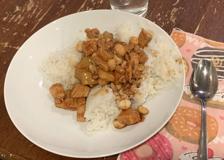Image shows the brown colored mix served over white rice on a white plate beside a pink donut napkin and spoon. 