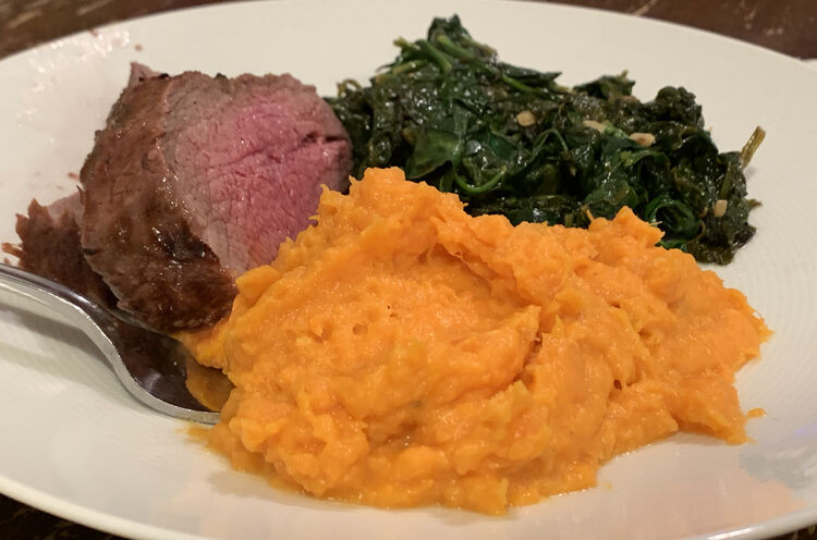 Closeup of a plate with three piles centered in the middle. On the left is perfectly made two thick slices of tri-tip, a pile of green, and, in the front, a pile of the recipe:  Coconut and Sweet Potato Mash.