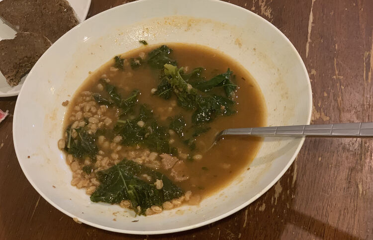 Image shows a bowl half filled with the brown soup with greens. You can see how high the soup used to be by the markings on the side. 