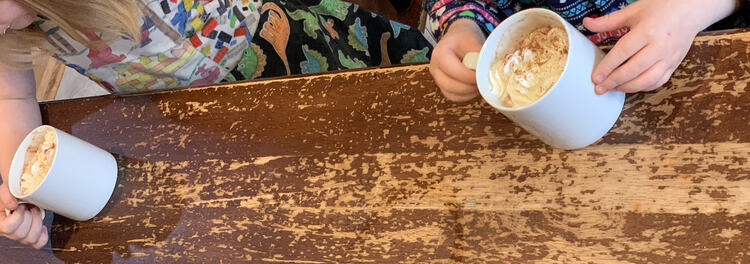 Image is taken from above looking down at the kids' mugs of hot chocolate and whip cream.