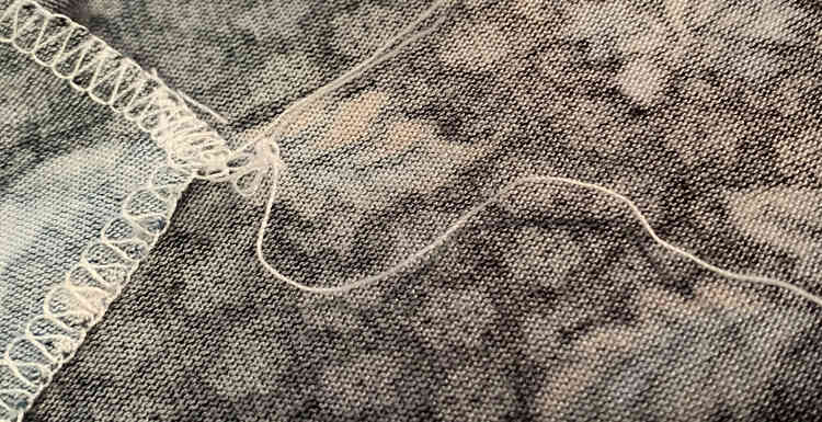 Image shows the thread tail completely unraveled although the seam on the fabric is still intact. The one loosened thread is going across the photo while the upper two are going up off the photo. 