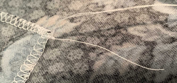 Image shows the two long thread tails going up and off the photo while the shorter one is pointed down more. At the base, against the seam and fabric, there's a small knot keeping it all together. 