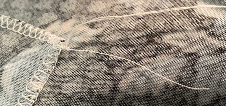 Image shows the two long thread tails going up and off the photo while the shorter one is pointed down more. At the base, against the seam and fabric, there's a small knot keeping it all together.