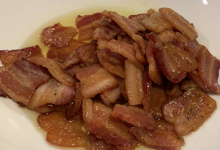 A closeup photo of a pile of incredible bacon sitting in a bit of liquid within a white bowl.