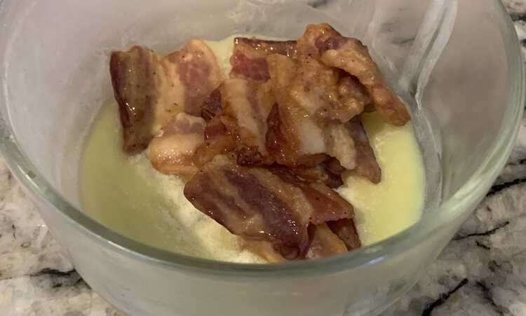 Image shows about ten pieces of bacon congealed from the cold fridge sitting in a glass container on the counter. 