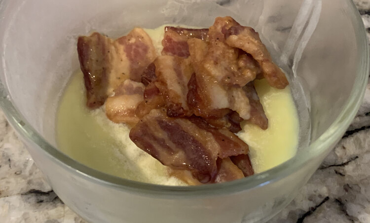 Image shows about ten pieces of bacon congealed from the cold fridge sitting in a glass container on the counter.