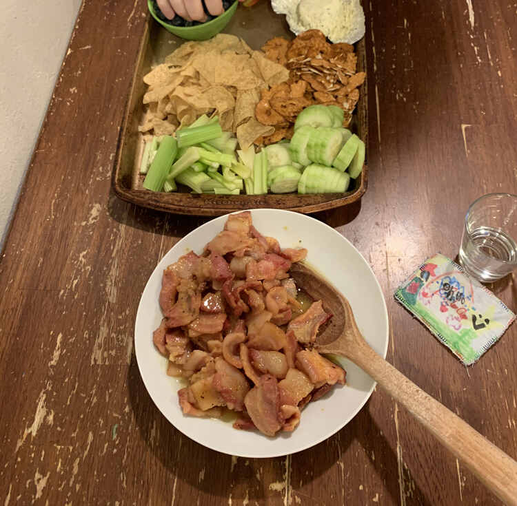 Image shows a bowl of the bacon bites with a wooden spoon for dishing. Off in the back is a cookie sheet covered in simple snacking yumminess. 