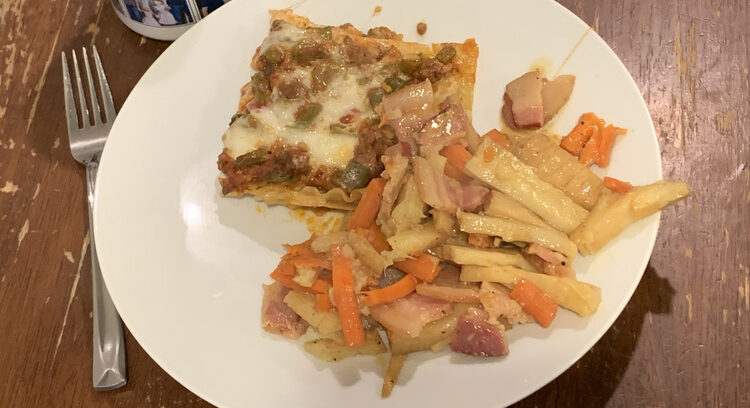 Image shows a square of lasagna sitting next to a pile of white, orange, and bacon. 
