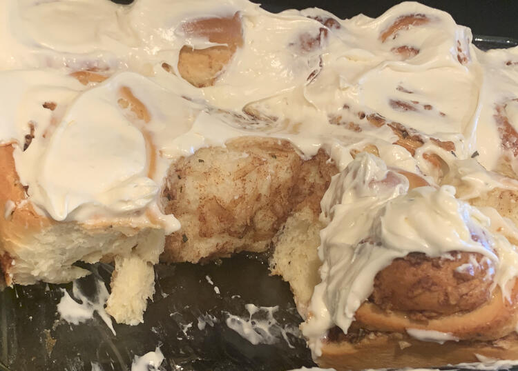 Image shows the white frosting coated cinnamon buns with a couple missing showing off the soft and fluffy interior. 