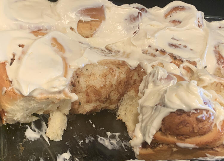 Image shows the white frosting coated cinnamon buns with a couple missing showing off the soft and fluffy interior.