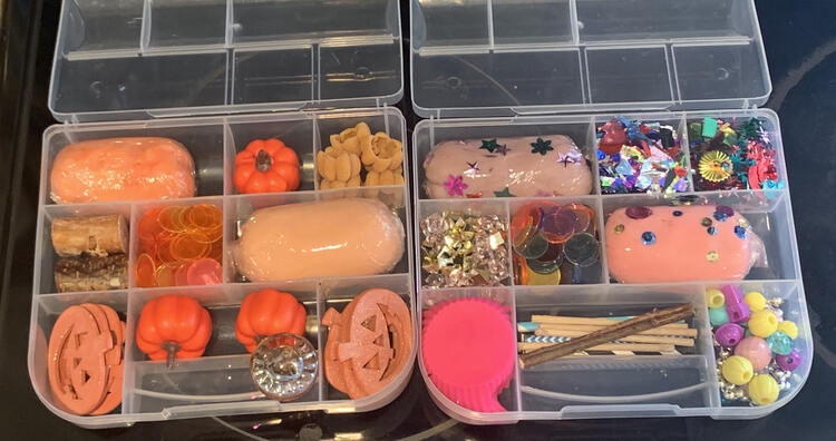 Two divided plastic containers sit out on the black stovetop. On the left sits the orange themed one while the cupcake and popsicle one is on the right.