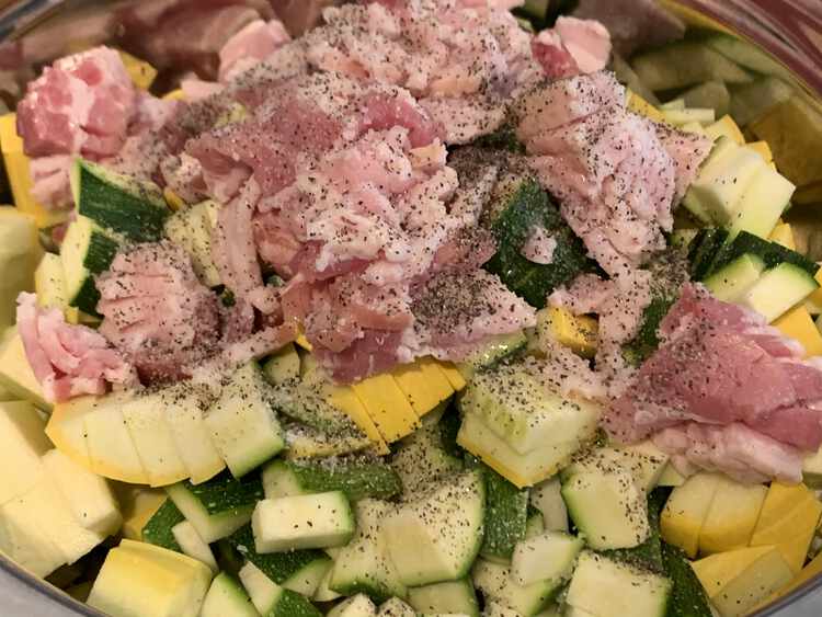 Image shows bacon sitting on top of diced yellow and green squash. The top is covered in pepper, visible, and salt, invisible to the image.