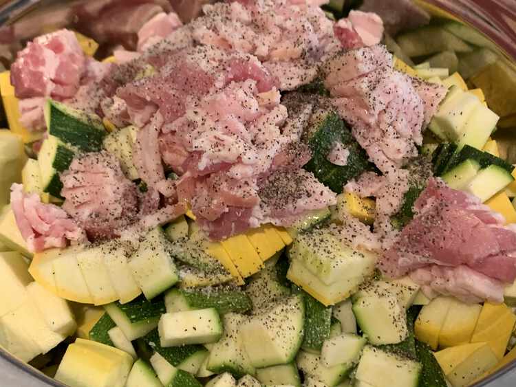 Image shows bacon sitting on top of diced yellow and green squash. The top is covered in pepper, visible, and salt, invisible to the image. 