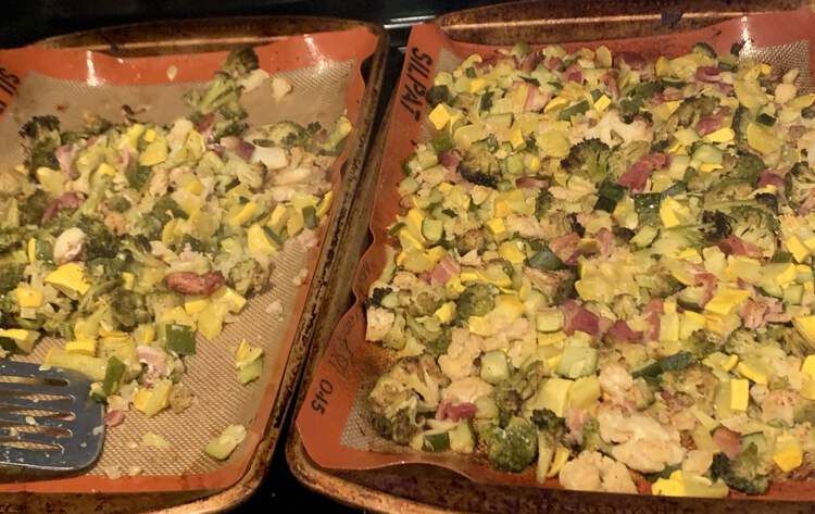 Image shows two cookie sheets side by side mostly coated in roasted bacon, cauliflower, broccoli, and squash. The left side is only half filled and a metal flipper lays across it testament to the fact that some has already been removed. 