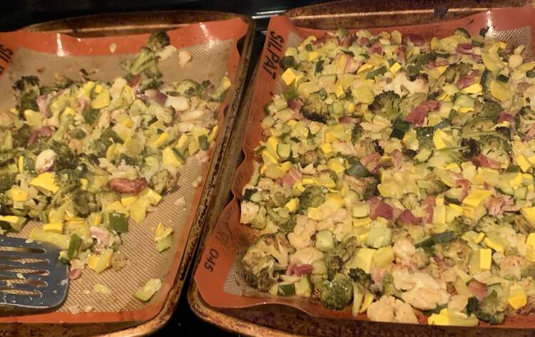 Image shows two cookie sheets side by side mostly coated in roasted bacon, cauliflower, broccoli, and squash. The left side is only half filled and a metal flipper lays across it testament to the fact that some has already been removed.