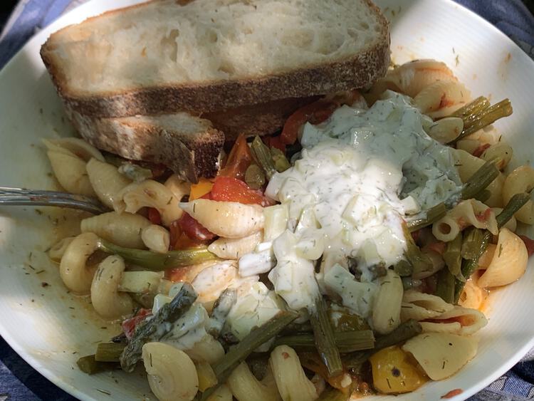 Image shows a white bowl filled with pasta, asparagus, popped cherry tomatoes, tzatziki, and, off to the side, two slices of amazing bread. 