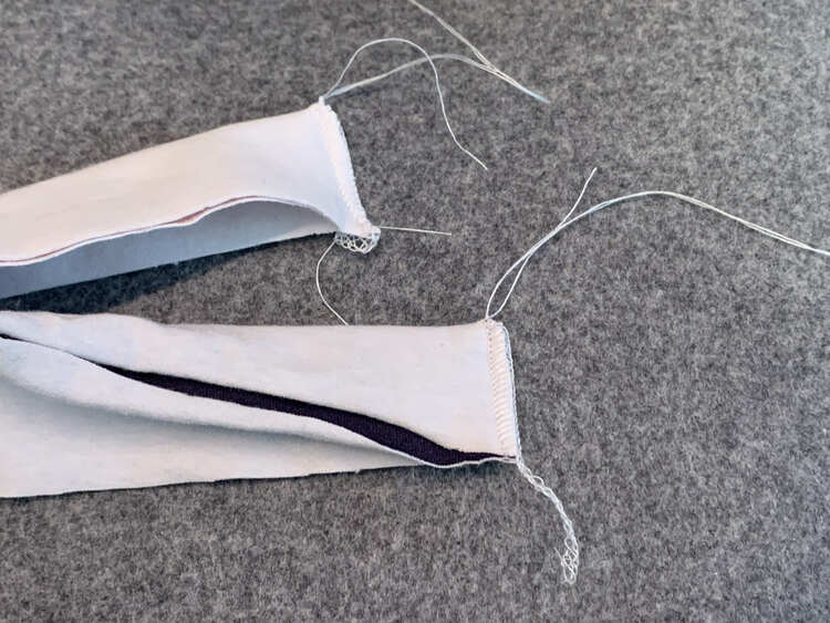 Image shows the serged ends of two different bands. Either one has a serger tail coming from the raw end while the top side, folded edge, has an unraveled tail with a knot at the base. 