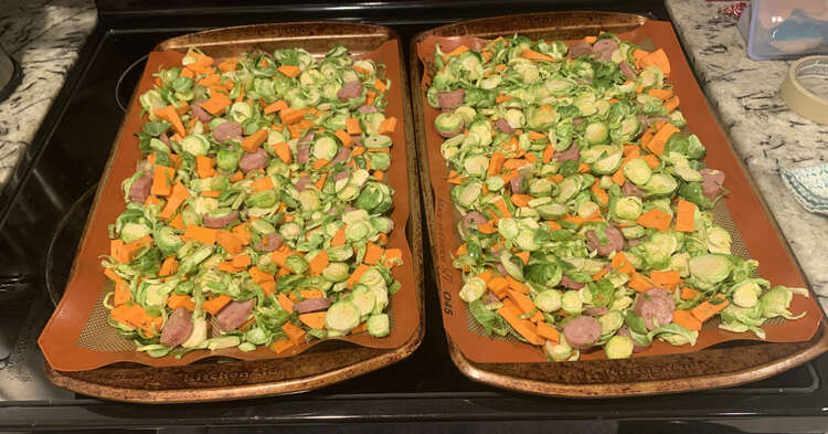 Image shows two cookie sheets laid side by side on top of the stove. They're both covered in the green, orange, and pinkish-brown food. 