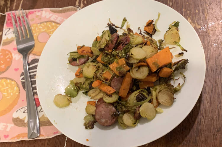 Plate with a mix of greens, yams, and sausages. A nakin and fork lay to the left.