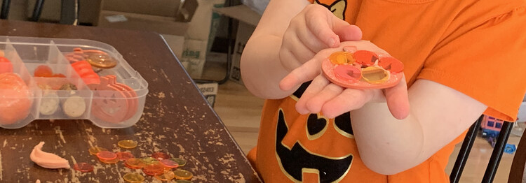 Image shows Zoey holding a glittery wooden pumpkin with plastic bingo disc 'glued' on with playdough.
