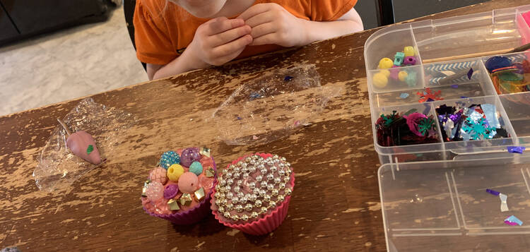 Image shows two playdough filled cupcake liners decorated with beads. To the left sits an purple popsicle on plastic wrap. To the right sits the opened kit. 