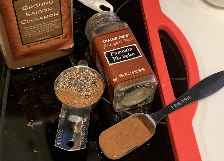 Image shows a 1/8 cup measuring cup, and empty pumpkin pie spice jar, cinnamon, and a tablespoon. The measuring cups and spoon have brown and black spices in it.  