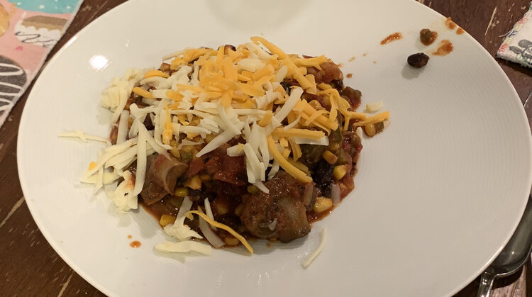 Image shows a plate with a mound of chili in the center covered in little pieces of orange and white cheese. 