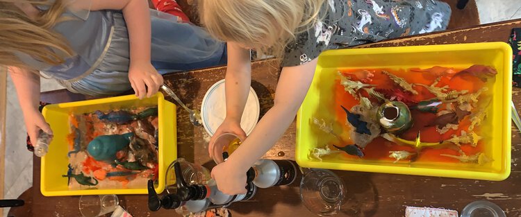 Ada's volcano has blue lava coming out while Zoey pumps yellow dye into her plastic cup.