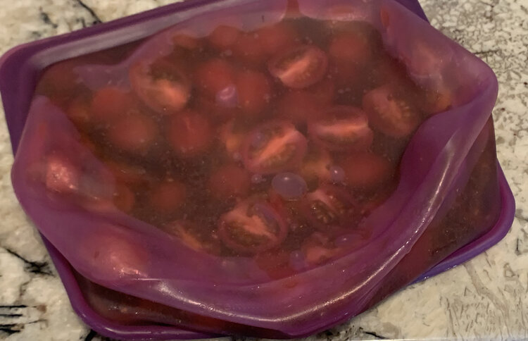 Image shows a squished purple bag on it's side on the counter. You can see halved tomatoes in a liquid as the odd bubble is apparent.