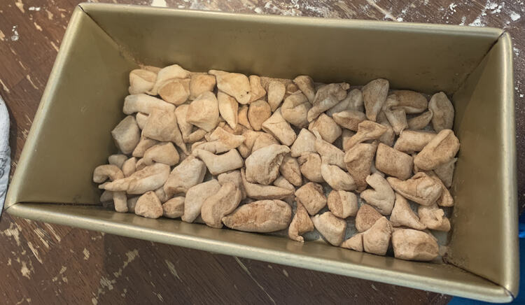 Image shows a loaf pan with a shallow layer of cut up dough scraps. 