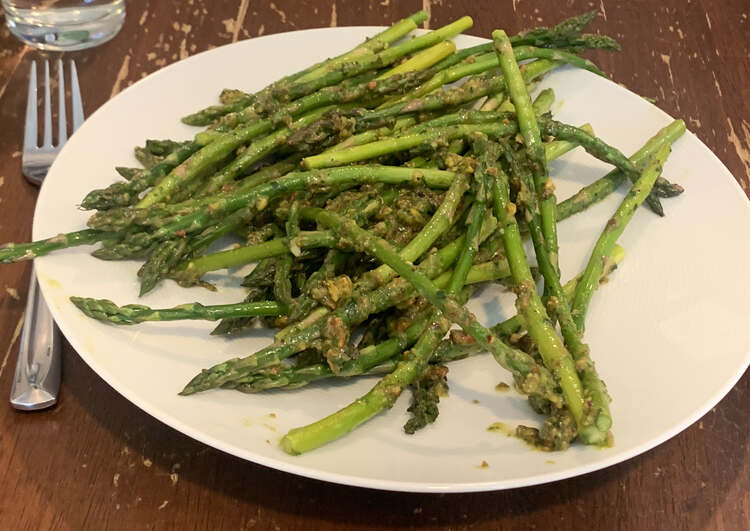 Image shows a white plate stacked with pistou coated asparagus. A fork is laid to the left. 
