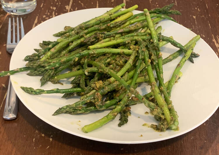 Image shows a white plate stacked with pistou coated asparagus. A fork is laid to the left.