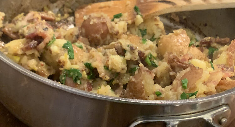 Image shows a closeup of a half filled skillet with a wooden utensil sitting inside to dish with.