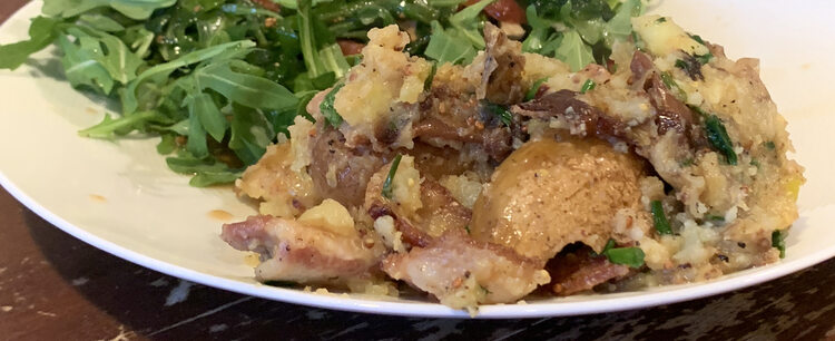 Image shows a closeup of my white plate with the potato dish on it. In the background you can see the arugula- based salad. 