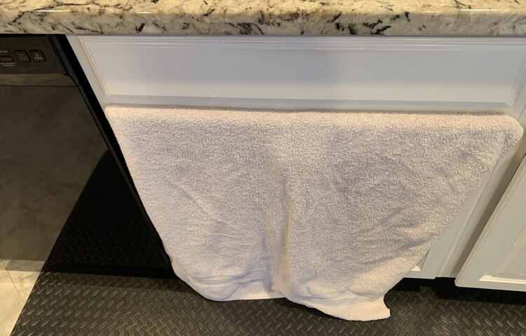 Image shows a white towel sticking out of the top of the under-sink cupboard and falling to the floor. 