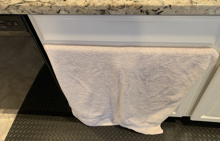 Image shows a white towel sticking out of the top of the under-sink cupboard and falling to the floor.