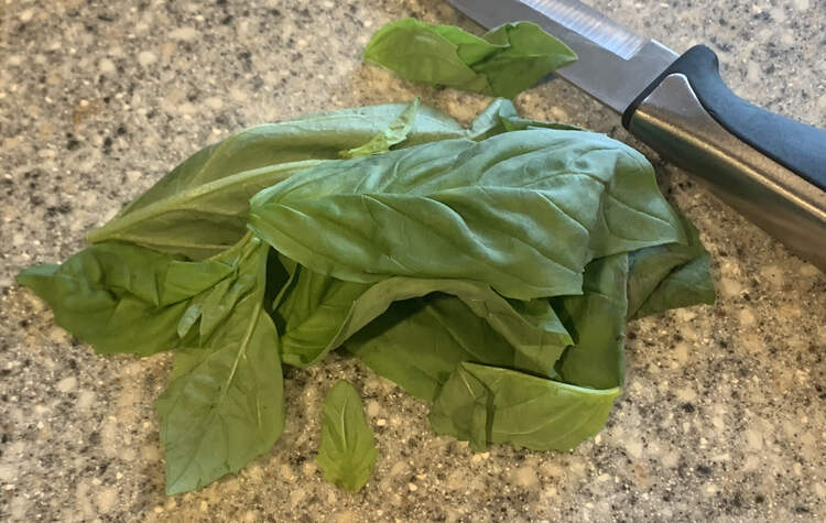 A pile of fresh basil set on a marble cutting board with a knife next to it. 