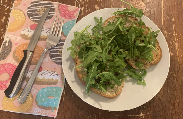 image shows two pieces of rye bread covered in leafy green arugula. You can see the odd dark splash of the balsamic vinegar that was sprinkled over top. 