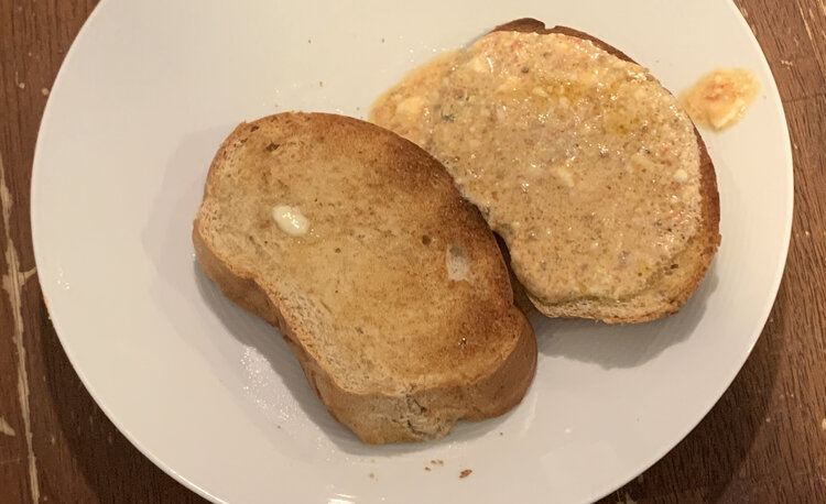 Two slices of rye toast sitting on a white plate. The one on the right is coated in a beige sauce with the odd white bit while the other was buttered with one little piece unmelted. 