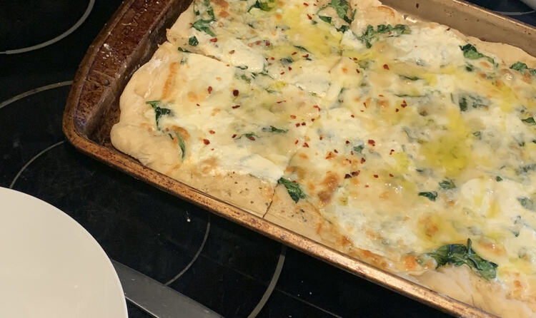 Image shows the final browned pizza sitting on a cookie sheet with the end cut into two pieces. A plate rests beside the cookie sheet. 