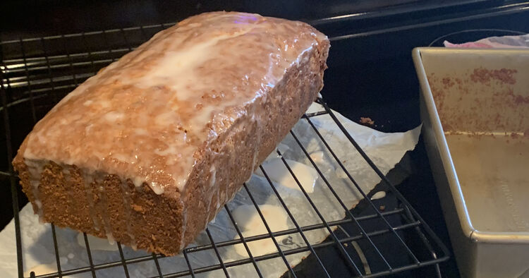 Image shows the loaf as one piece only with white dripping off it's ends on to the parchment below the cooling rack. Beside it sits a dirtied but emptied loaf pan.