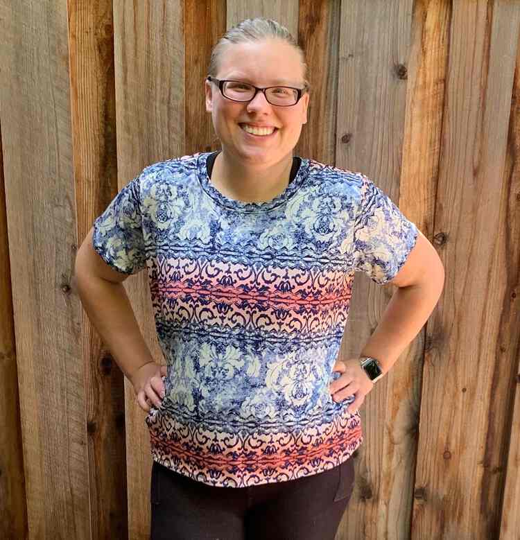 Me, a white woman, smiling with my hands on my waist facing the camera in front of my wooden fence.