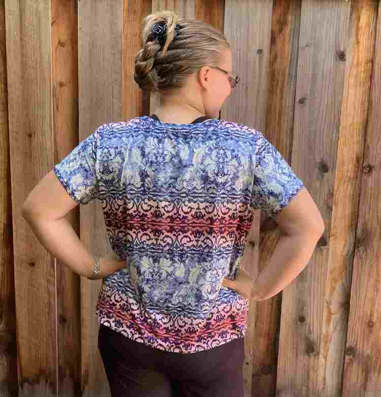 Me, a white woman, with my back to the camera as I face the wooden fence. My head is turned to the right and my hands are on my waist. The shirt is draping down from the shoulders and then bunched in at the waist under my hands.