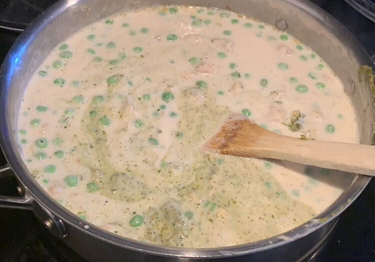 Image shows the top of the deep frying pan with a white mixture, floating green balls, and green flecks being mixed in with a wooden spoon. 