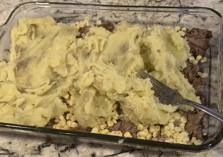 Image shows most of a glass casserole dish taken from above and looking down. Most of it is covered with mashed potatoes but you can see the corn covered meat along the one end and some of the sides. 
