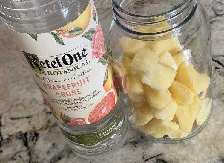 Image shows a bottle of Ketel One Botanical Grapefruit & Rose distilled vodka next to a clear canning jar partially filled with frozen pineapple chunks.  