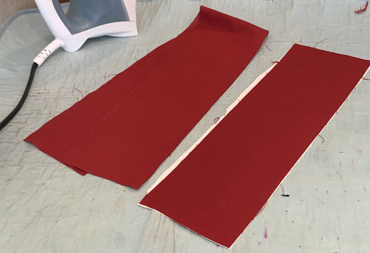 Image shows two red pieces of fabric on a blue faded ironing mat with an iron behind it.