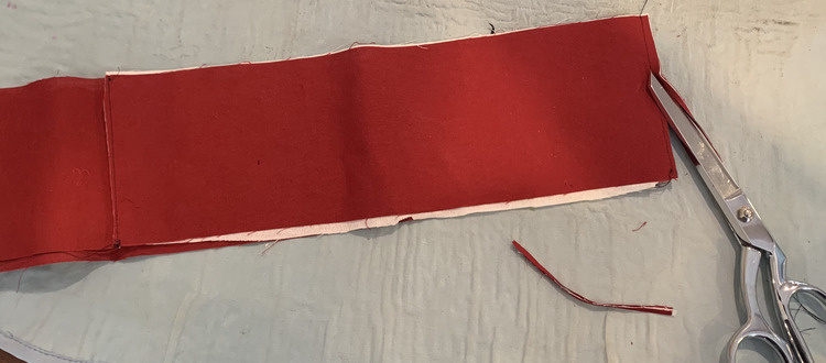 Image shows the waistband with the rightmost seam being trimmed, with the scissors laying on the pressing mat, and the left seam facing up and already trimmed.